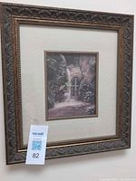 Full view of framed print on wall showing frame, mat, print, and lot tag