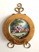 Front view of porcelain plate in metal frame showing pastoral scene and gold border