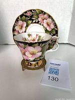 Teacup nested in saucer on brass stand showing floral pattern and gold trim