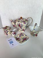 Full set showing teapot, sugar bowl, spoon, creamer, teabag rest, basket