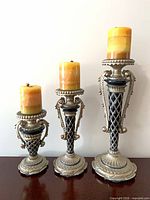 Three ornate antique silver candle holders with candles, front view