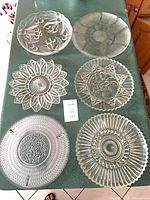 Group shot of six clear pressed glass plates displaying varied patterns