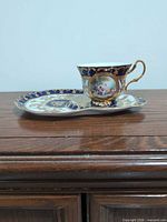 Cup on snack saucer showing cobalt blue, gold gilt, and figural scene