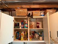 Overall view of open wall cabinet showing cleaners, glass items and wicker baskets