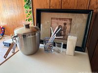 ice bucket, tongs, rocks glass, shot glass, stirrer box and straws visible
