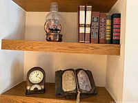 Shelf view showing oil lamp sconce, book volumes, book sculpture and Seiko clock