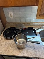 All pans, saucepan, strainer on countertop