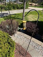 Two black metal shepherd hooks with yellow tube bird feeder in background