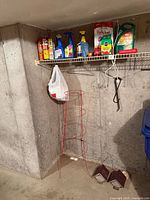 Overview of shelf with garden chemicals, red tomato cage, birdhouses on floor