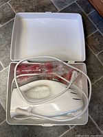 Hamilton Beach handheld appliance inside white plastic case with cord and accessories