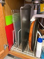 Full lot in cabinet showing plastic boards, cooling racks, baking sheet, pizza pans, wooden board, organizer