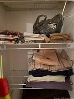 Two shelves holding folded sheets, towels, holiday linens in plastic bag