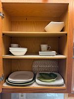 Cabinet shelf view showing stacked plates, bowls, mug, leaf dish, glass platter