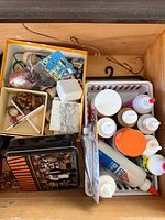 Drawer view showing mixed craft supplies: adhesives, tins, wood beads, hooks