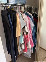 Closet rod with mix of slacks, pastel sweaters, patterned shirts and garments in dry-clean bag