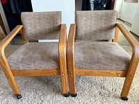 Front view of two oak frame armchairs showing upholstery and casters