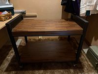 Front view of rolling cart showing two dark wood shelves and black frame on casters