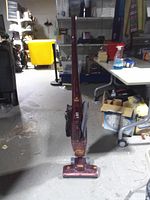 Full view of burgundy Bissell stick vacuum standing upright