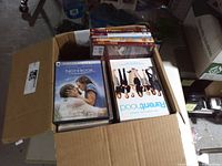 Open box showing assorted DVD cases with visible titles The Notebook, Parenthood, Mary Poppins