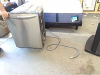 Front and side view of dishwasher showing handle, door and attached hose