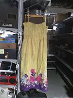 Full view of yellow smocked maxi dress hanging, showing floral hem and straps
