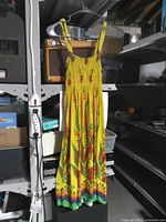 Full view of yellow sleeveless smocked floral garment hanging on hanger