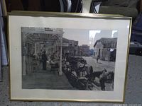 Framed monochrome print of frontier street with horses and wagons