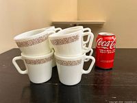 Stacked view of all eight mugs beside soda can for scale