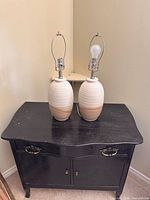 Two ceramic lamps on dark cabinet, front view