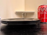Stack of four black octagonal plates beside soda can for scale