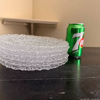 stack of six clear pebble-texture plates beside 355 mL 7-Up can for scale