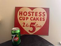 Full view of Hostess Cup Cakes tin sign with 7-Up can for scale