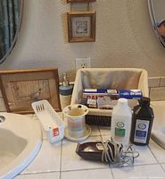 All items on countertop: clipper, bottles, basket with toiletries, framed prints, soap dispenser, tumbler, caddy
