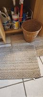 Two beige chenille rugs on tile floor with wicker wastebasket