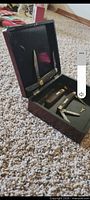 Open wood case showing both folding knives seated in lid and base, small brush and key visible