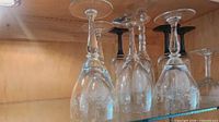 Several upside-down clear glass wine glasses on shelf