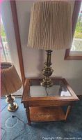 Side table with glass top and tall brass lamp on it; shorter lamp visible
