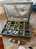 Open jewelry box displaying assorted costume jewelry pieces and coin charm bracelet