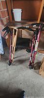 Folded pink/magenta rollator walker with black seat and wood accessory board