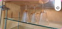 Four inverted amber-tinted wine glasses on glass shelf