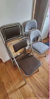 Stack of six folding chairs showing both brown vinyl and gray fabric variants