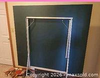 Front view of folding table half against wall, metal legs visible, paddles at base