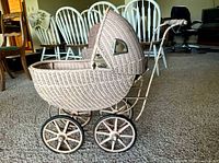 Left side view of wicker doll pram showing wheels, frame, hood