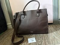 Front view of dark brown faux leather handbag with strap and logo visible