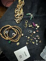 Layout of entire lot on black surface showing chain, bracelets and earrings