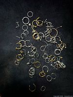 Overview of mixed gold and silver body jewelry pieces scattered on dark surface