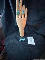 Wooden hand display showing two turquoise rings and pair of turquoise earrings