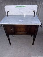 Full view of washstand showing marble top, backsplash, brass arms, wood base, towel bar and legs