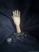 Rings displayed on wooden mannequin hand and scattered on surface