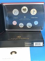 Open presentation book showing encapsulated 7-coin set and COA card